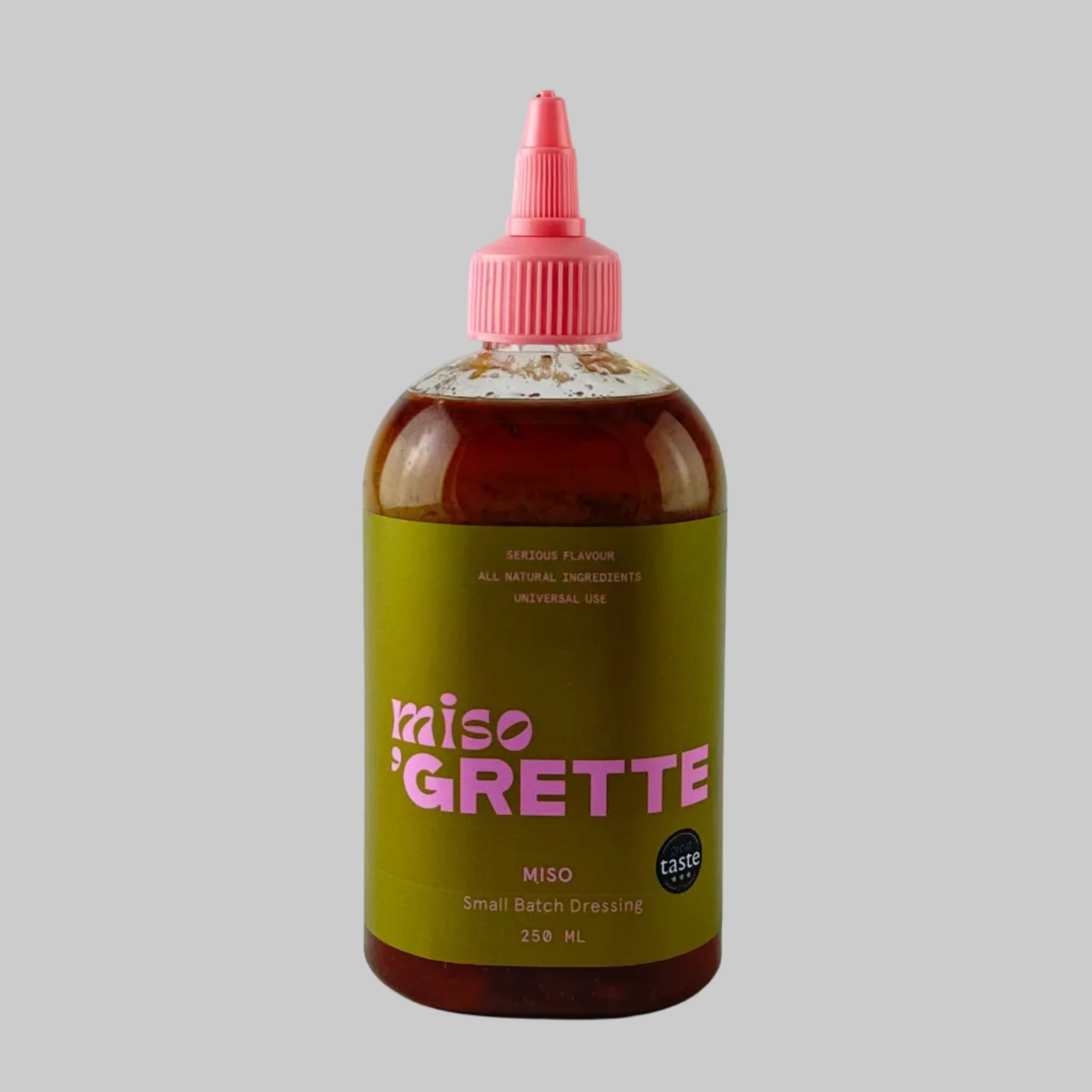 Bottle of miso dressing from Grette with a green and pink label on a grey background